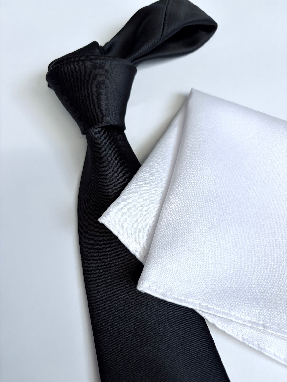 Black tie and white pocket square on a light background