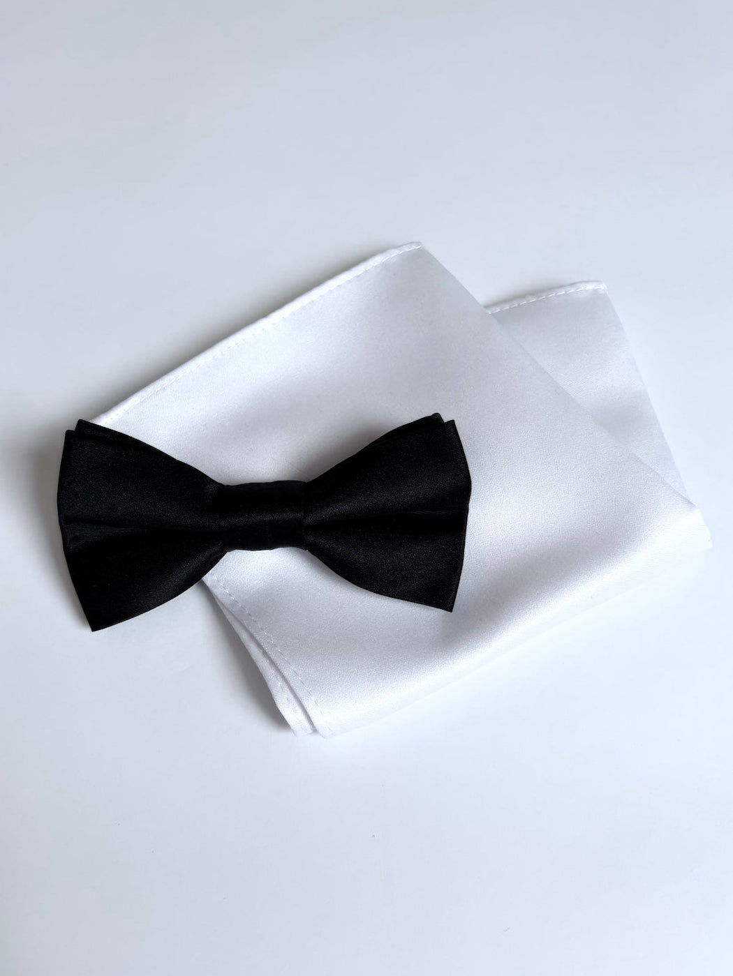 Black bow tie and white pocket square on a light background