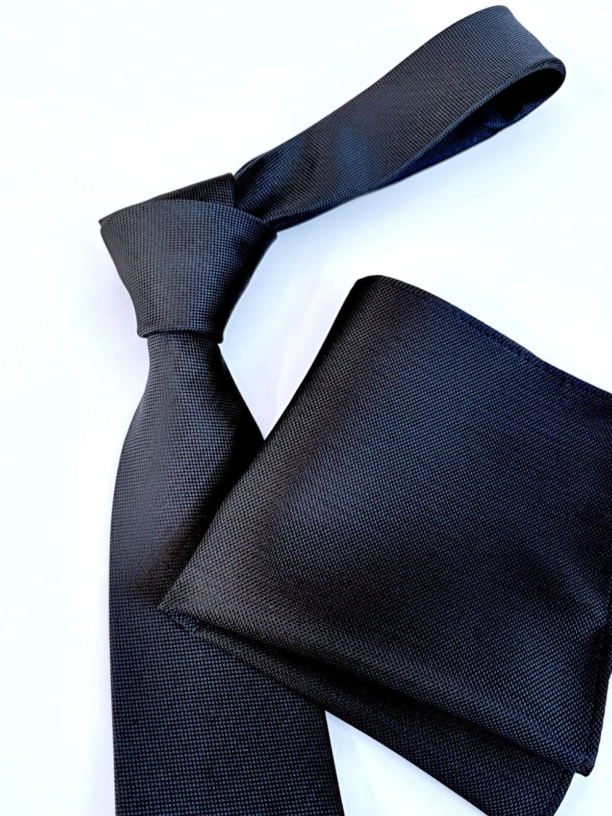 A dark navy textured necktie and matching pocket square set, neatly arranged on a clean white background.
