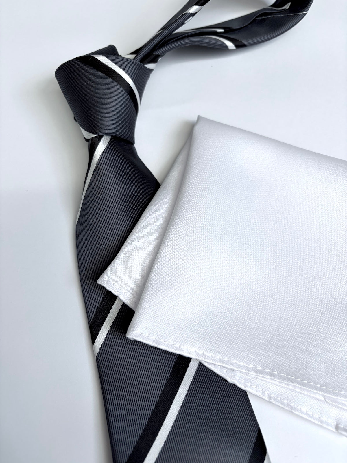 Charcoal striped tie and white pocket square on a light background
